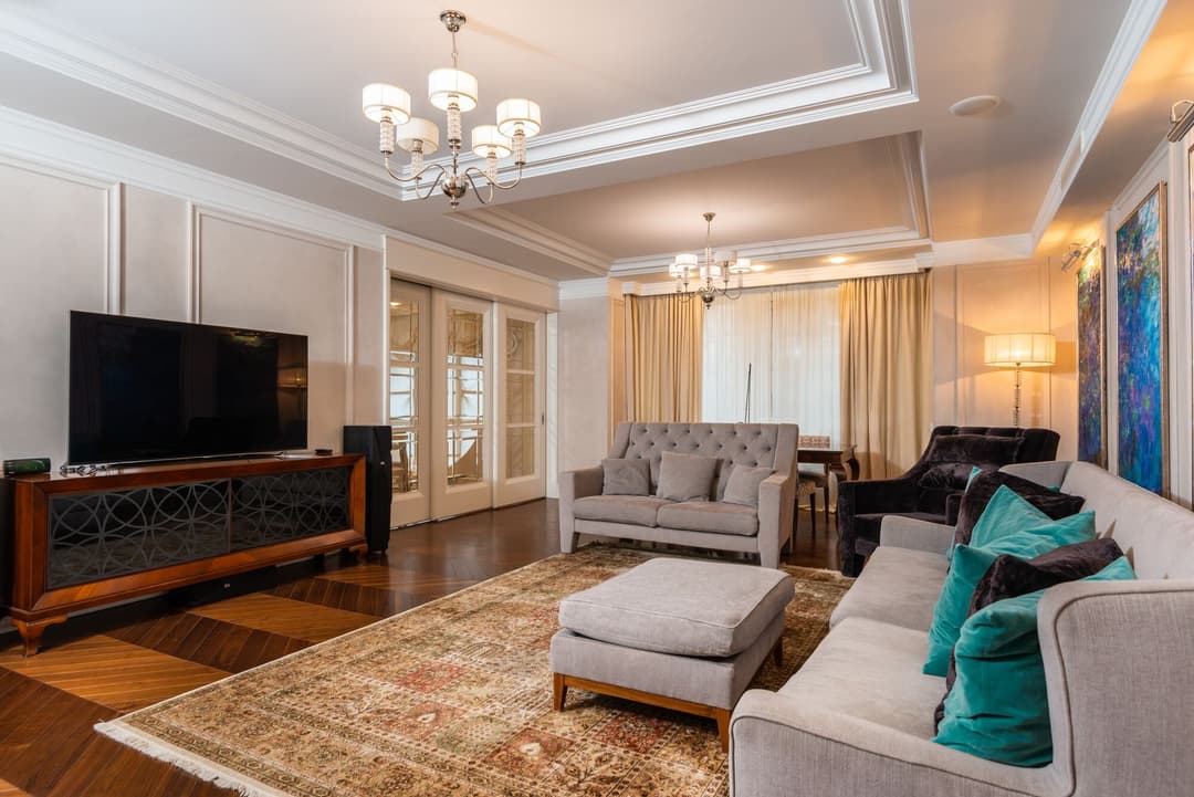 A living room lit in layers: a chandelier, cove light in the ceiling, and a lamp beside the sofa