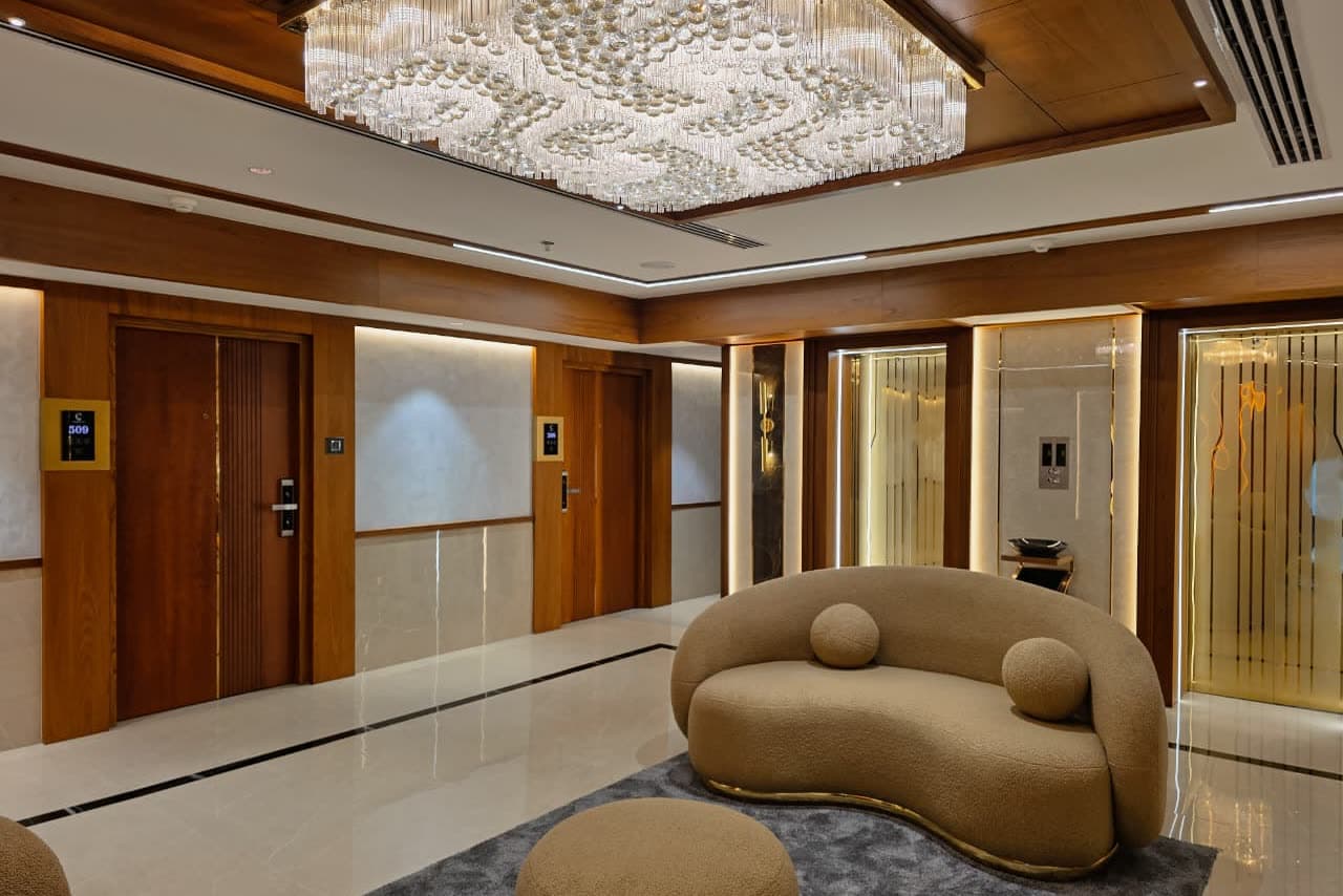 A lift lobby with a wide crystal ceiling fixture and backlit panels